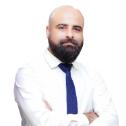 Prof Faizan Ali in white shirt and blue tie with arms crossed against plain white background