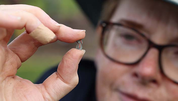Dr Michelle Comber holding a turquoise and red glass bead found at the Rathgurreen Ringfort and beli