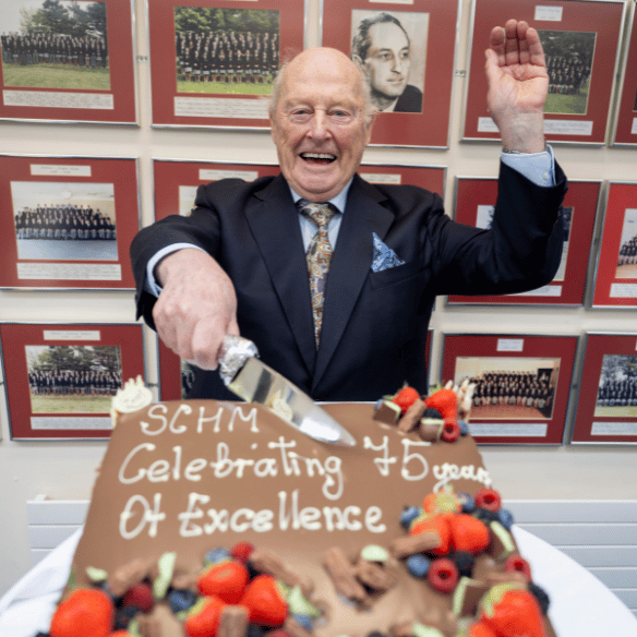 Older gentleman and alumni smiling and cutting celebratory cake 