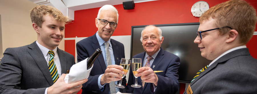 new head of college and retired head of college, smiling with two students 